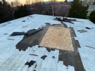 Roof with large sections of shingles torn away by wind, decking exposed to weather